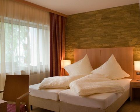 Doppelzimmer im Gaestehaus Birkenhof was die  Dependance des Weinhotel Kaisergarten darstellt hier Blick auf das Doppelbett und Schreibtisch mit Stuhl. 