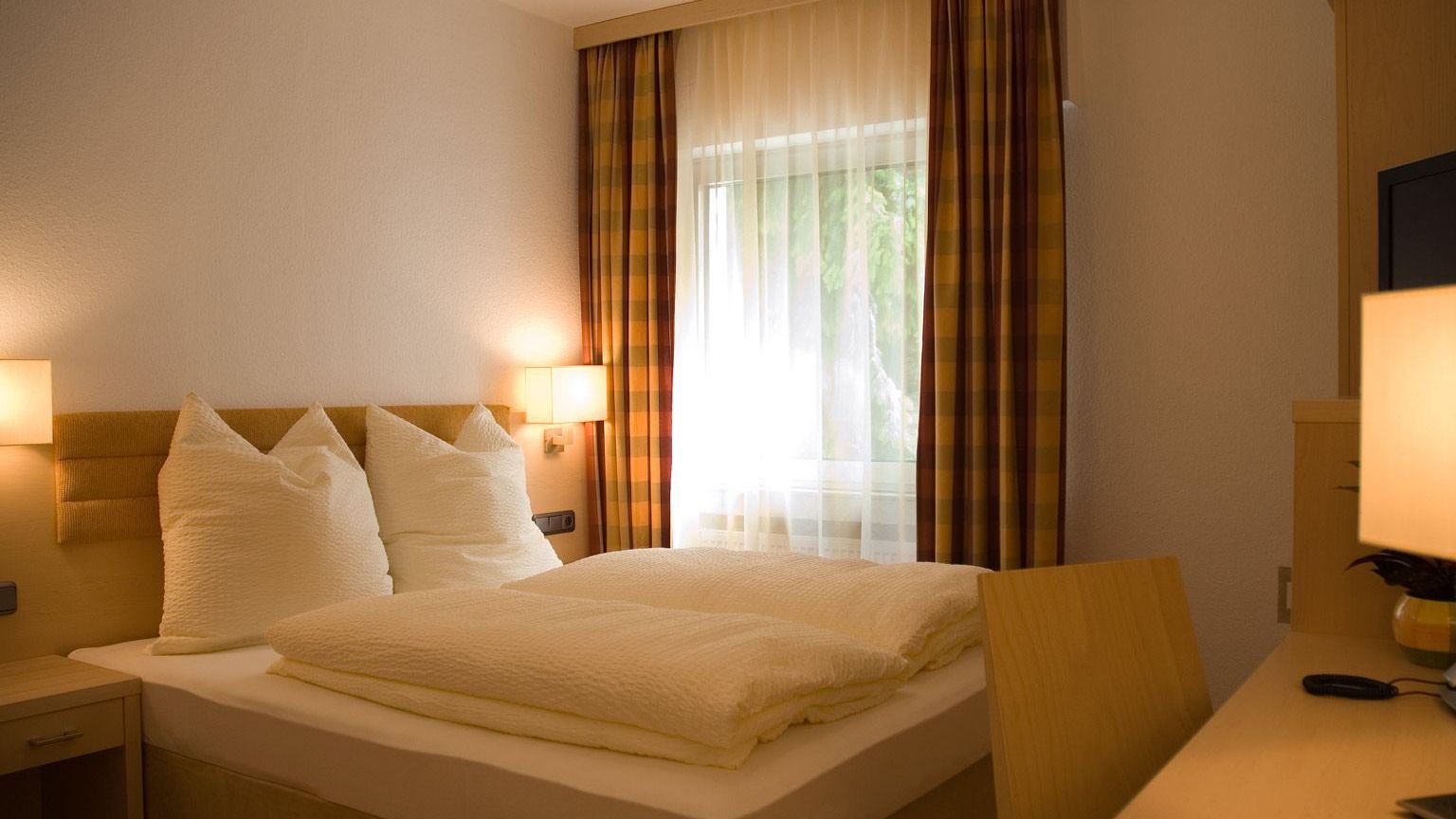 Doppelzimmer im Gaestehaus Birkenhof was die  Dependance des Weinhotel Kaisergarten darstellt hier Blick auf das Doppelbett und Schreibtisch mit Stuhl.  